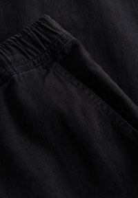 Sort stof med fiskebensmønster, der har en elastisk talje og en glat tekstur, vist i et nærbillede.