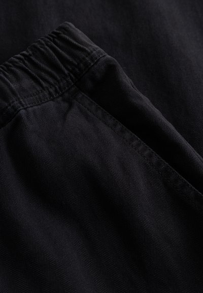 Tissu noir avec un motif en chevrons, doté d'une ceinture élastique et d'une texture lisse, présenté en gros plan.