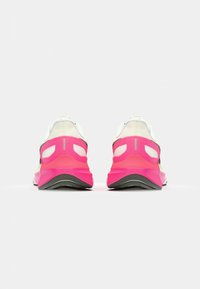 Chaussures de course avec un dessus blanc, des accents rose et noir, et une semelle texturée. Elles présentent un talon rembourré et un matériau en mesh respirant.