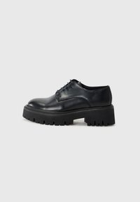 Chaussure en cuir noir à lacets avec une pointe arrondie, une épaisse semelle de plateforme noire et des détails texturés sur le bord de la semelle.