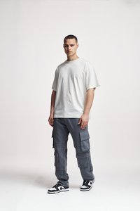 Tricou crem cu mânecă scurtă, croială lejeră, asortat cu pantaloni cargo gri cu multiple buzunare, completat cu adidași negri și albi.