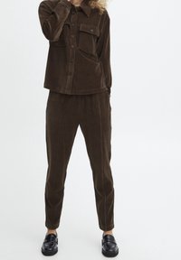 Bruine corduroy overhemd met knoopsluiting en twee borstzakken, gecombineerd met bijpassende bruine corduroy broek. Gladde textuur en aangesloten ontwerp.