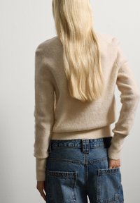 Maglione di lana beige con un bordo a coste aderente, abbinato a pantaloni cargo in denim blu con ampie tasche e vita alta.