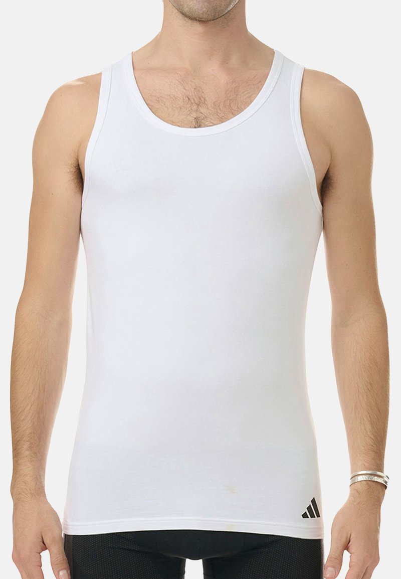 Vitt atletiskt linne med breda axelband, tillverkat av ett glatt tyg. Har en svart Adidas-logotyp på nedre vänstra sidan.