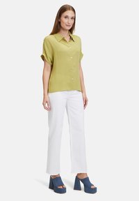 Olive green short-sleeve button-up shirt, paired with white wide-leg pants and blue denim platform heels. Smooth fabric and relaxed fit.
