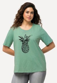 Grünes T-Shirt mit kurzen Ärmeln aus leichtem Stoff, mit einem schwarzen Ananas-Grafikdesign, das mittig auf der Vorderseite platziert ist.