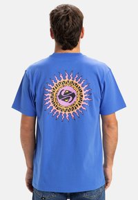 Blaues Baumwoll-T-Shirt mit einem runden, mehrfarbigen Sonnengrafik auf dem Rücken, die sich windende Strahlen und ein zentrales Logodesign zeigt.