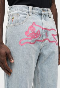 Ανοιχτό μπλε τζιν με ροζ σχέδιο παιδικής γάτας στον μηρό, με ένα μικρό κεντητό εικονίδιο παγωτού στην μπροστινή τσέπη.