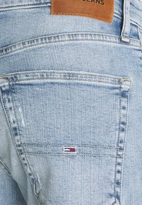 Helle blaue Denim-Jeans mit einem braunen Lederaufnäher am Bund und einem kleinen gestickten Etikett mit rot-, weiß- und blauen Streifen.