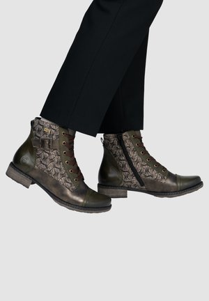 Ankle-high lace-up boots with side zipper and buckle, featuring dark green leather and patterned fabric panels, worn with black pants.