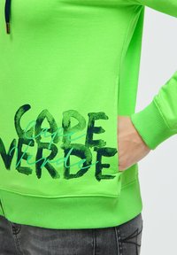 Neongrüner Pullover mit einer strukturierten Aufschrift "Kap Verde", ausgestattet mit einer Kängurutasche und gerippten Bündchen. Weiches Baumwollmaterial.