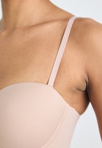 Light pink bra with molded cups, adjustable straps, and a smooth texture. Strap features subtle logo detailing.