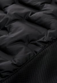 Tessuto in nylon nero imbottito con sezioni trapuntate, superficie liscia e lucida e un bordo testurizzato nero, che mette in evidenza diverse texture.