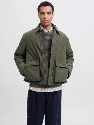 Olive green puffer jacket with a collared neckline, front snap closure, and two large front pockets, layered over a gray sweater and white shirt.