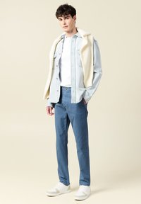 Ljusblå denimskjorta över en vit T-shirt, matchad med blå byxor och vita sneakers. Anmärkningsvärda detaljer inkluderar en strukturerad, krämfärgad tröja.