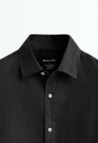 Chemise en lin noire à boutons avec col, trois boutons blancs visibles et étiquette de marque cousue à l’intérieur de l’encolure.