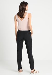 Černé kalhoty na míru s elegantním střihem a bočními kapsami, doplněné o světle růžový top bez rukávů s vykrojením na zádech. Jednoduché ploché sandály.