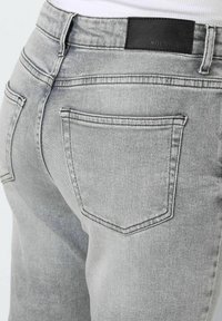 Jeans de mezclilla gris con una vista en primer plano de la parte trasera, que presentan una etiqueta de cuero negro y bolsillos estándar, mostrando una textura suave.