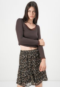 Brun langermet croppet topp med dyp utringning, kombinert med et svart og brunt mønstrete skjørt med elastisk midjebånd og lagdelt design.