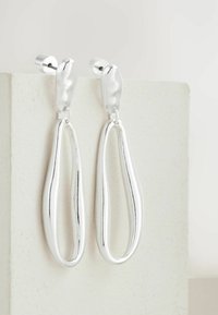 Silberne Tropfenohrringe mit elongated Loop-Design, polierter Oberfläche und sicherem Postverschluss, auf einem hellen Hintergrund präsentiert.