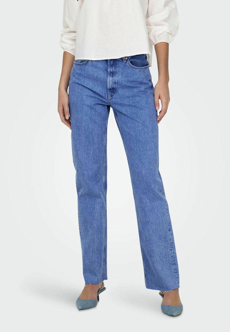 Niebieskie dżinsy o prostym kroju, z klasycznym pięcioma kieszeniami i średnim stanem, w zestawieniu z jasnoniebieskimi butami.