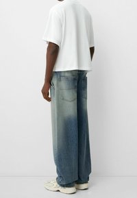 Vit kortärmad t-shirt i cropped modell, kombinerad med ljusblå, vida jeans med en urblekt mönstring och två bakfickor. Vita sneakers fulländar looken.