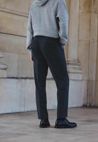 Pelēka kapucīna džemperis, melni svītraini bikses un melnas kurpes. Dizainā ir relaksēta piegriezuma un smalka tekstūras kontrasts uz auduma.