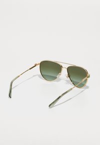 Kuldseid aviator-prille roheliste läätsedega, saledast metallraamist, tekstureeritud detailidega ja rohelise tooni käsitsemisega. Säästvad ninapadjakesed on lisatud.