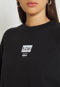 Felpa nera con scollo a girocollo, caratterizzata da un logo Levi's bianco e elementi di design in azzurro chiaro e bianco sul petto.