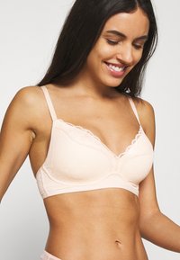 Bralet din dantelă roz deschis, cu un model floral, cu cupe cu padding și bretele ajustabile. Prezintă o margine din dantelă ondulată de-a lungul liniei gâtului.