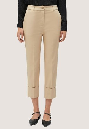 Beige op maat gemaakte cropped broek met omslagzomen, gedragen met zwarte puntige enkelriem schoenen en een zwarte, getextureerde lange mouwen top.