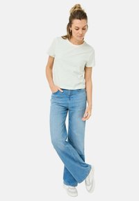 Stribet lyseblå og hvid bomulds t-shirt parret med høj talje lyseblå denim flared jeans og hvide sneakers.