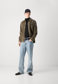 Corduroy olive shirt, black turtleneck, light blue wide-leg jeans, black belt, and black boots. Casual outfit with textured details.