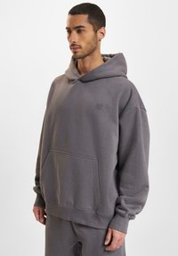 Gray hoodie made from soft material, featuring a front pocket, drawstring hood, and subtle branding on the chest. Loose fit and ribbed cuffs.