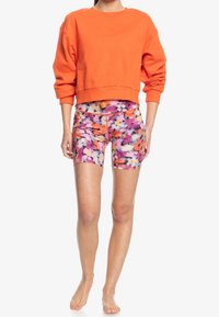 Sudadera corta naranja con puños acanalados y pantalones cortos con estampado floral en rosa, naranja y blanco. Textura suave, diseño ajustado, hasta la rodilla.