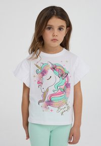 T-shirt bianca a maniche corte con grafica di un unicorno, criniera colorata, glitter e testo "Nato per brillare". Materiale in cotone liscio.