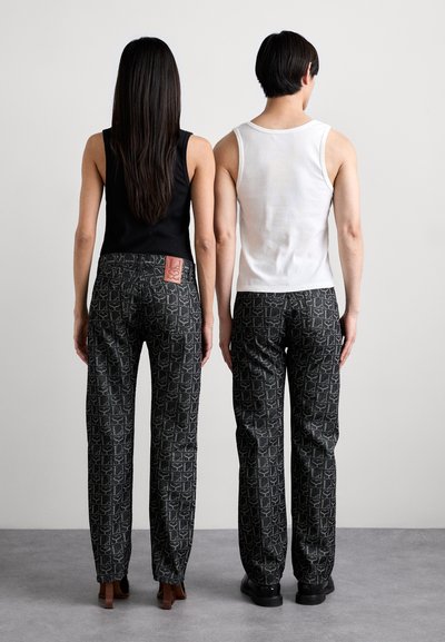 Un pantalon à motifs noir et blanc avec une étiquette rouge à l'arrière. Porté avec un débardeur noir et un débardeur blanc, tous deux ajustés.