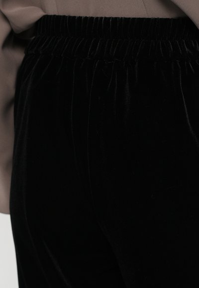 Les pantalons en velours noir sont dotés d'une ceinture élastique côtelée, d'une texture douce et d'une coupe fuselée, mettant en avant le confort et la facilité de port.