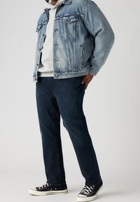 Vaaleansininen farkkutakki harmaan hupparin päällä, yhdistetty tummansinsisiin farkkuihin ja mustiin matalavartisiin lenkkareihin, joissa on valkeat pohjat.