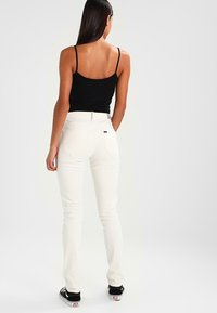 Jean en denim blanc à coupe slim, avec des poches arrière et une légère élasticité. Associé à un débardeur noir et des baskets noires.