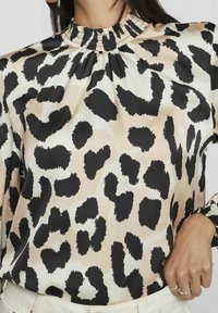 Blouse à imprimé léopard avec un col montant à volants, présentant une texture satinée en beige et noir, à manches longues et coupe décontractée.