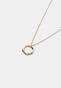Goldene Anhänger-Halskette mit einem welligen, unregelmäßigen kreisförmigen Design, das an einer feinen, zarten Kette hängt. Glatte, glänzende Oberfläche.