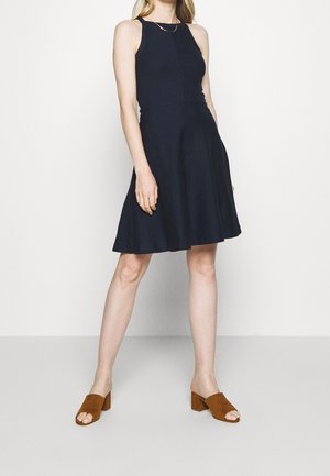 Laivastonsininen hihaton mekko, jossa istuva vartaloalue ja levenevä helma, valmistettu sileästä kankaasta. Yhdistetty ruskeisiin mokkanahkanutek korollisiin mules-sandaaleihin.