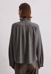 Grijze gestreepte blouse met een hoge geplooide kraag, luchtige mouwen en een geplooide achterkant. Het materiaal lijkt zacht met subtiele textuurvariaties.