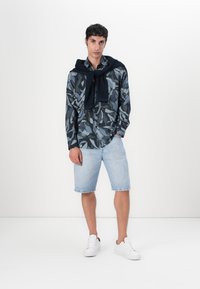Langermet marineblå skjorte med bladmønster, kombinert med lyseblå denimshorts. Hvite sneakers fullfører antrekket.