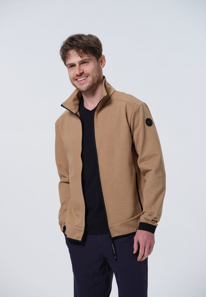 Chaqueta tipo sudadera de color marrón con cuello alto y puños acanalados, hecha de una tela suave. Presenta un parche con logo negro en el hombro izquierdo y bolsillos con cremallera.