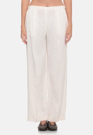 Pantaloni bianchi a gamba larga con pieghe frontali e vita con coulisse, indossati con scarpe marrone scuro su una persona in piedi.