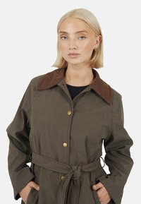 Cappotto leggero verde oliva con colletto in corduroy marrone, chiusure a bottone e cintura. Presenta maniche lunghe e tasche laterali.