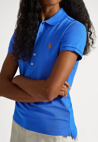 Μπλε πόλο πουκάμισο από υφασμάτινη υφή με κλασικό γιακά, κοντά μανίκια και κεντημένο πορτοκαλί λογότυπο στο αριστερό στήθος.