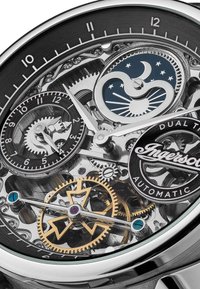 Automatisch horloge met een transparante behuizing, zilveren tandwielen, een zwarte wijzerplaat, blauwe accenten en een dubbele tijd subdial met gouden en paarse details.
